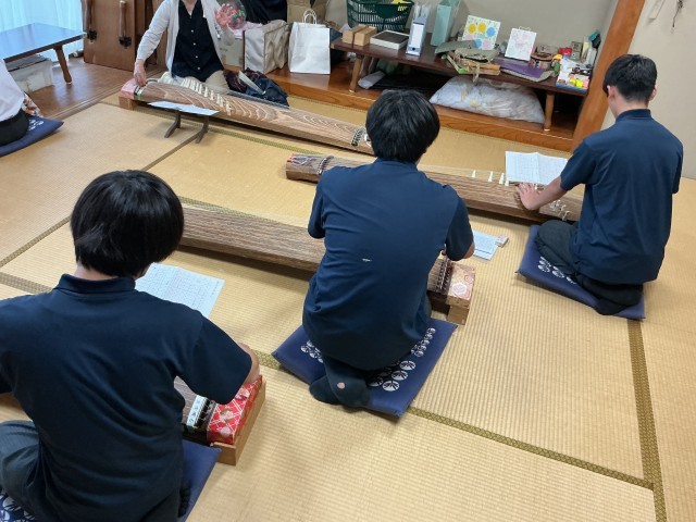 3年生3名が和室に座り、前に箏の先生が座り、全員で箏の稽古をしている場面