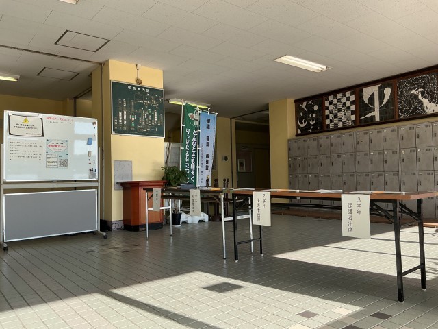 昇降口に置かれた受付台とホワイトボードの案内表示